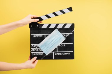 Sarı renkli, sinema konseptine izole edilmiş alkış tahtası ve tıbbi maskeli kamera asistanı görüntüsü.