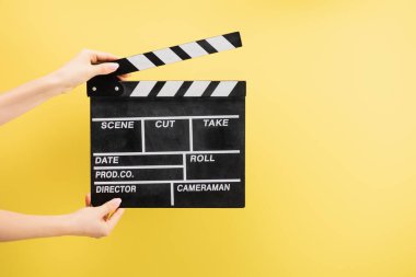 partial view of camera assistant holding clapperboard isolated on yellow, cinema concept clipart
