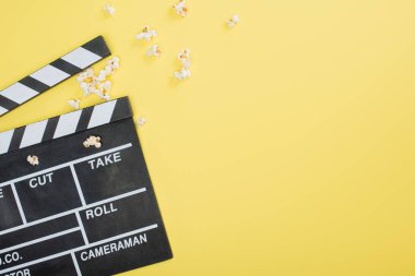 top view of clapperboard near scattered popcorn on yellow, cinema concept clipart