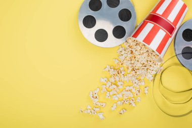 Kovanın yanındaki film makaralarının en üst görüntüsü sarı üzerine patlamış mısır serpiştirilmiş sinema konsepti.