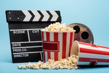Clapperboard, film makarası ve kovalarla mavi üzerine patlamış mısır, sinema konsepti