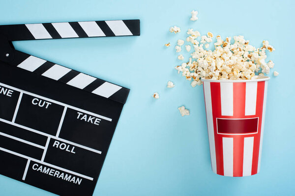 верхний вид полосатого ведра с попкорном рядом с доской на голубом, концепция кино