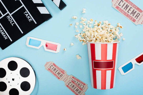 top view of clapperboard, 3d glasses, cinema tickets, film reel and bucket of popcorn on blue