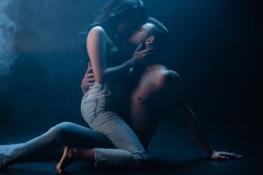Kot pantolonlu ve sütyenli seksi kadın siyah arka planda erkek arkadaşını öpüyor. 