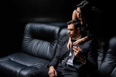 Kanepenin yanındaki çekici kadının yanında elinde viski bardağı tutan bir adam. 