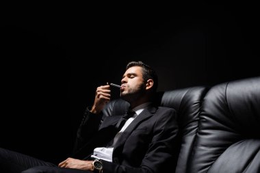 Sigaranın yanında elinde çakmak tutan takım elbiseli adam siyah koltukta izole edilmiş. 