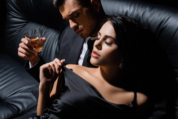 Мужчина держит стакан виски рядом с чувственной женщиной на диване 