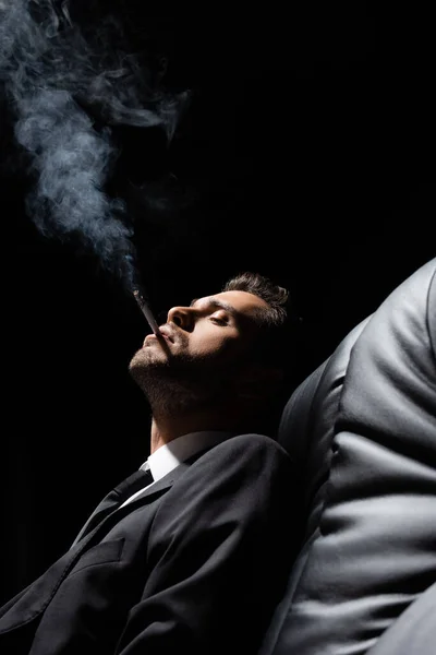 Young Man Suit Smoking Cigarette Couch Blurred Foreground Isolated Black — Stock Photo, Image