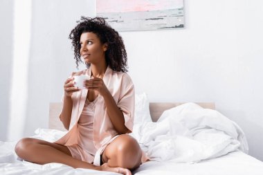 Kahve fincanı taşıyan Afro-Amerikalı bir kadın gözlerini yataktan ayırmıyor. 