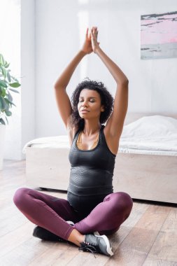 Hamile Afrikalı Amerikalı kadın yoga pozisyonunda yatak odasında yerde oturuyor. 