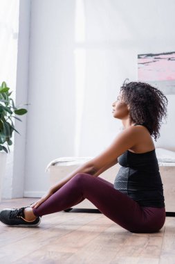 Hamile Afro-Amerikan sporcunun yatak odasında yerde oturması. 