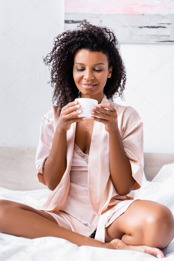 African american woman holding cup of coffee on bed 