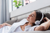 mírumilovná mladá dospělá žena se zavřenýma očima odpočívající ve sluchátkách na gauči doma