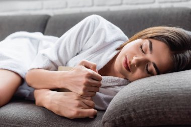 young adult woman sleeping with book in hands on grey couch at home clipart
