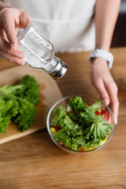 Genç yetişkin bir kadının taze sebze çeşnili salata ve tuz değirmeninin mutfağında kısmi görüntüsü