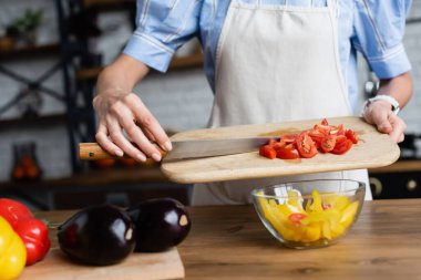 Genç yetişkin bir kadının modern mutfakta sebze salatasına dilimlenmiş kiraz domatesi koyması kısmi bir bakış açısı