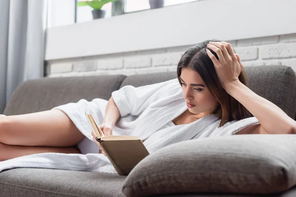 Serious Young Adult Woman Bathrobe Reading Book Grey Couch Home — Stock Photo, Image