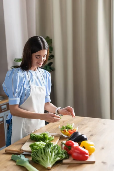 Sorrindo Jovem Mulher Adulta Avental Cozinhar Legumes Frescos Salada Cozinha — Fotografia de Stock