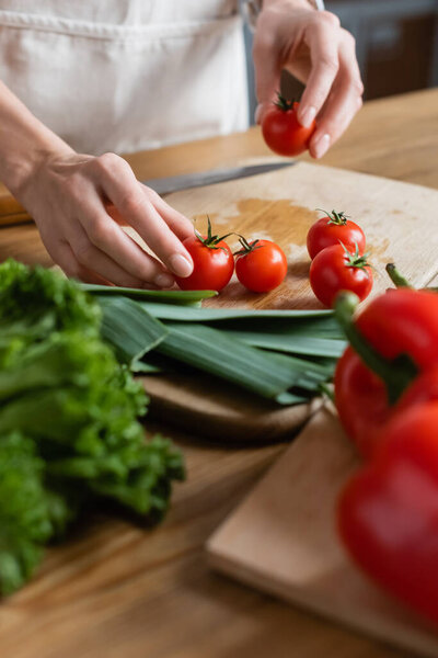 partial view of female hands holding cherry tomatoes on chopping board in modern kitchen