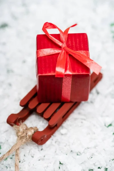 Caixa de presente vermelho com fita em trenó de madeira na superfície de neve decorativa — Fotografia de Stock