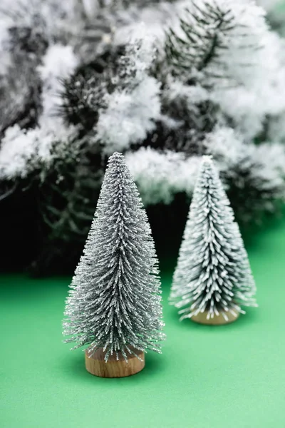 Arbres de Noël décoratifs et branche de sapin recouverte de neige sur vert — Photo de stock