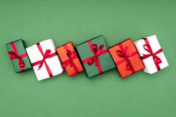 Top view of multicolored gift boxes with red ribbons on green background — Stock Photo