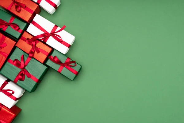 Top view of multicolored gift boxes with red ribbons on green background with copy space — Stock Photo