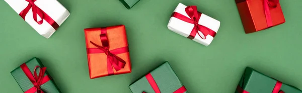 Panoramic shot of colorful gift boxes with red ribbons and bows on green background, top view — Stock Photo