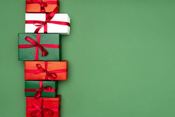 Top view of colorful gift boxes with red ribbons on green background with copy space — Stock Photo