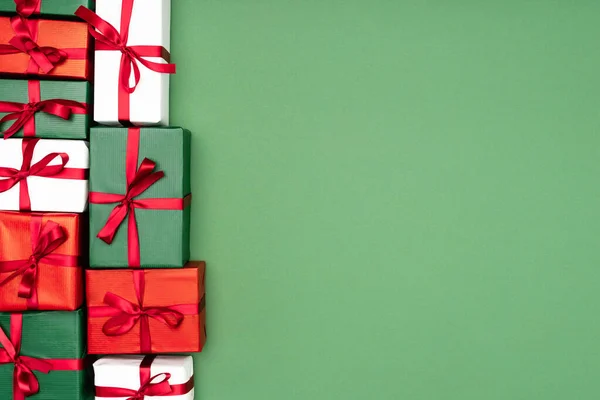 Top view of multicolored gift boxes with red ribbons on green background with copy space — Stock Photo