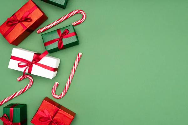 Top view of colorful gift boxes and candy canes on green background with copy space — Stock Photo