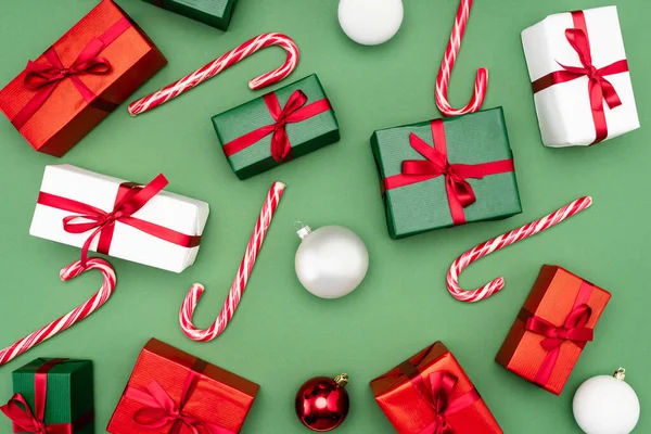 Top view of colorful gift boxes, candy canes and christmas balls on green background — Stock Photo