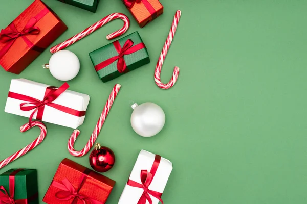 Vista dall'alto di scatole regalo multicolore, bastoncini di caramelle e palle di Natale su sfondo verde — Foto stock