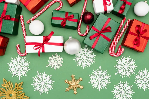 Vue de dessus des boîtes-cadeaux multicolores, des cannes à bonbons, des boules de Noël et des flocons de neige décoratifs sur fond vert — Photo de stock