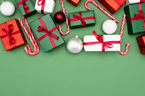 Vista superior de caixas de presente coloridas, bengalas doces e bolas de Natal no fundo verde com espaço de cópia — Fotografia de Stock