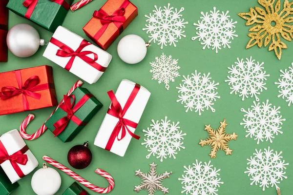 Top view of gift boxes, christmas balls, candy canes and decorative snowflakes on green background — Stock Photo