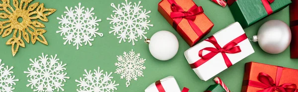 Tiro panorâmico de caixas de presente coloridas, bolas de Natal e flocos de neve decorativos no fundo verde, vista superior — Fotografia de Stock