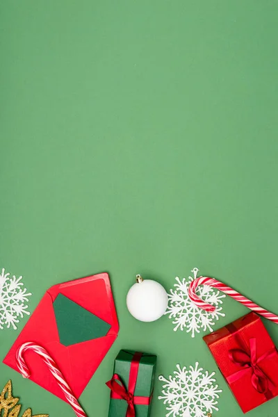 Ansicht der Geschenkbox, Umschlag mit Karte, Weihnachtskugel, Zuckerstangen und dekorativen Schneeflocken auf grünem Hintergrund mit Kopierraum — Stockfoto