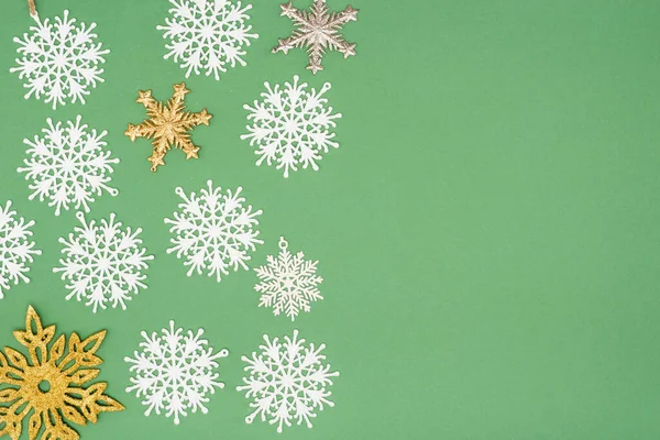 Vue de dessus des flocons de neige décoratifs blancs, dorés et argentés sur fond vert avec espace de copie — Photo de stock