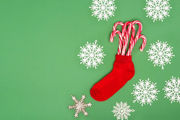 Media de Navidad roja con bastones de caramelo cerca de copos de nieve decorativos en verde - foto de stock