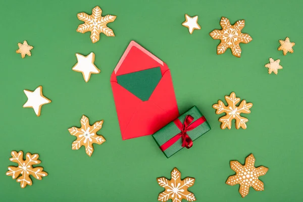 Vista superior del sobre rojo con tarjeta cerca de la caja de regalo, copos de nieve al horno y estrellas en verde - foto de stock