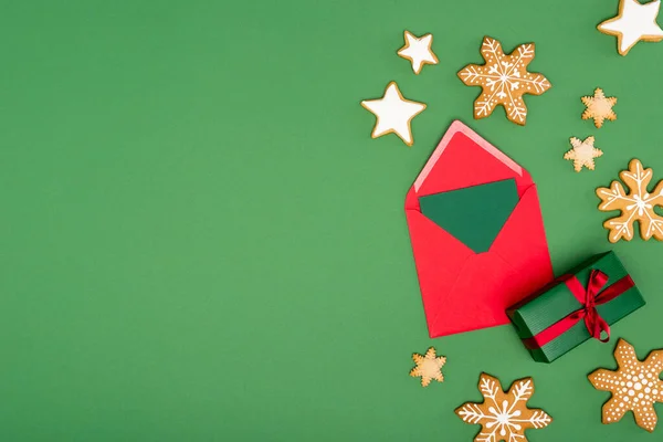 Top view of red envelope with card near baked snowflakes and stars on green background with copy space — Stock Photo