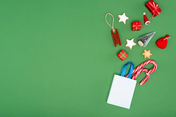 Einkaufstasche mit Zuckerstangen, Christbaumkugeln und Plätzchen auf grünem Hintergrund mit Kopierraum — Stockfoto