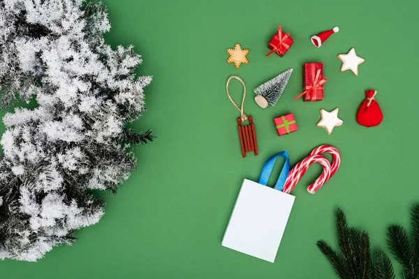 Vue du dessus du sac à provisions avec des cannes à bonbons près des boules de Noël et une couronne de pin avec de la neige décorative sur fond vert — Photo de stock
