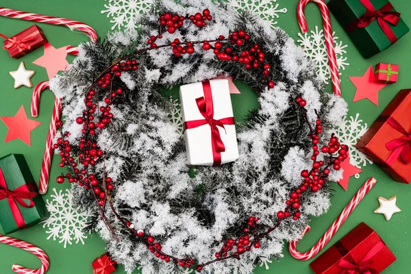 Top view of juniper wreath, covered with snow, near gift boxes and candy canes on green — Stock Photo