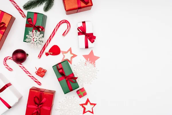 Vista superior de cajas de regalo, copos de nieve decorativos, galletas en forma de estrella y bastones de caramelo sobre fondo blanco - foto de stock
