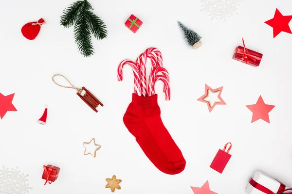 Calza di Natale rosso con bastoncini di zucchero vicino ai biscotti e bagattelle festive su sfondo bianco — Foto stock