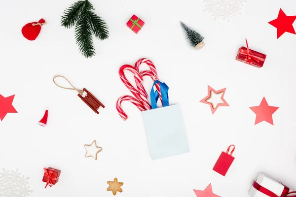 Saco de compras com bengalas doces perto de bugigangas de Natal e biscoitos no fundo branco — Fotografia de Stock