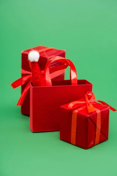 Boîtes-cadeaux rouges et sac à provisions avec chapeau de Père Noël sur fond vert — Photo de stock