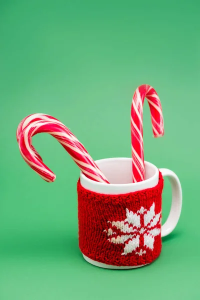 Dos bastones de caramelo en taza con portavasos de punto con copo de nieve sobre fondo verde - foto de stock